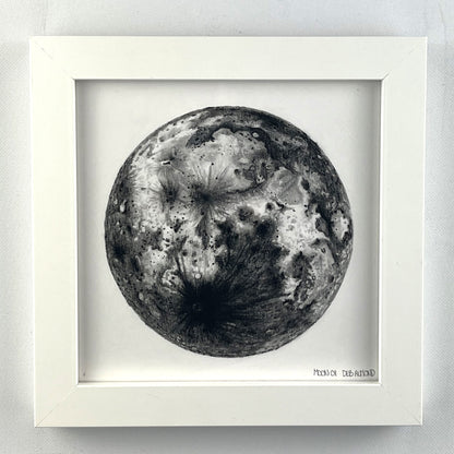 Framed drawing of the moon in black pastel pencil on white paper.